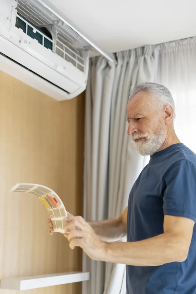 Signs That You Need AC Repair - Mature man with gray beard and hair checking air conditioner.