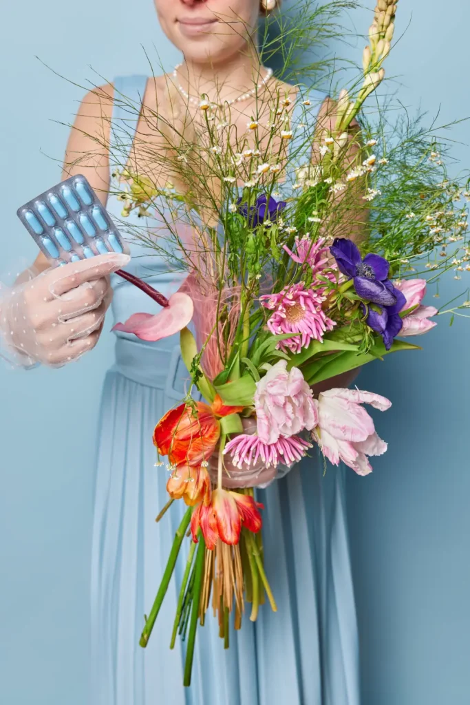 Cropped image of unrecognizable lady in dress holds pills and bouquet of wild flowers going to cure